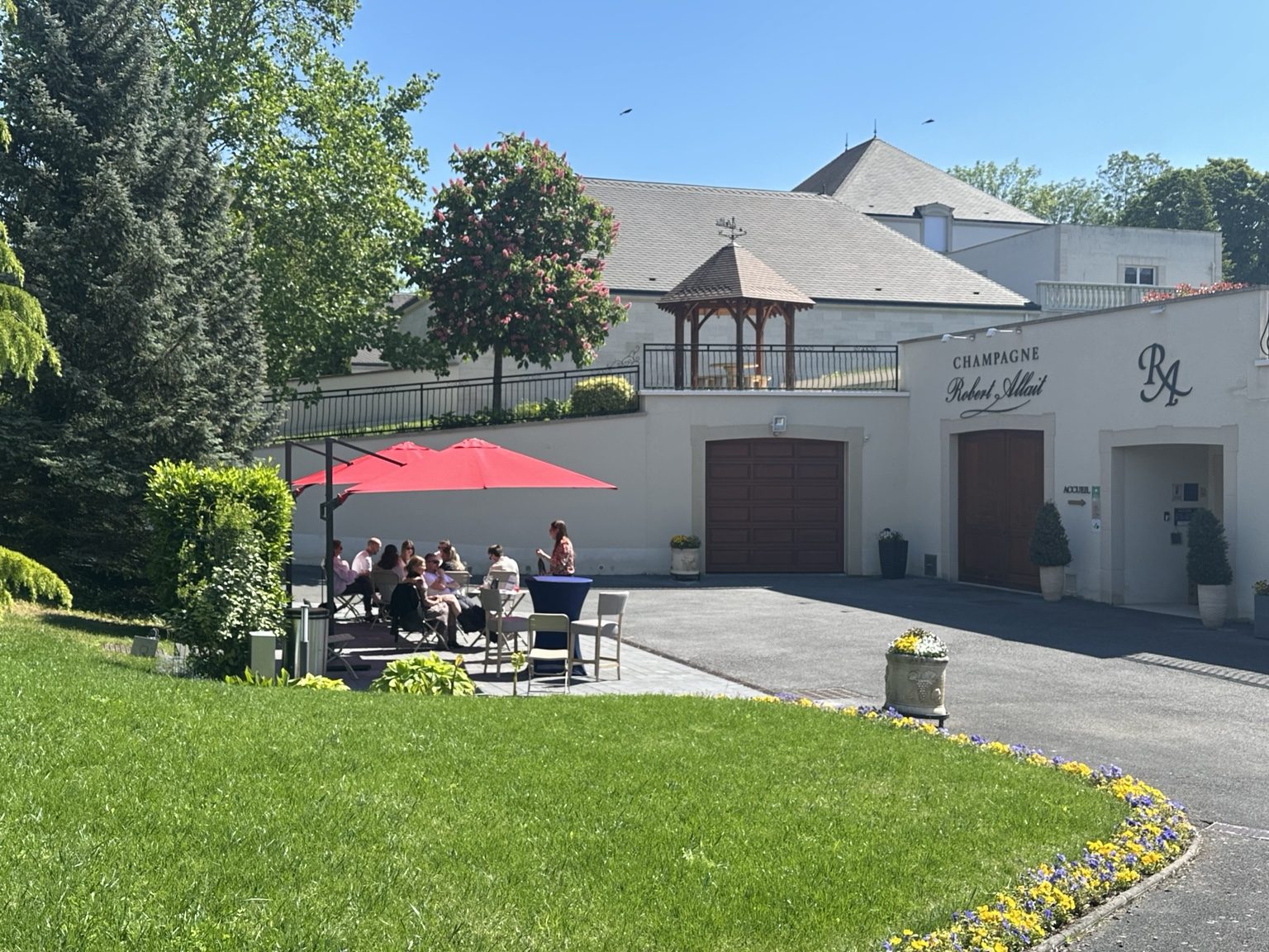 The Champagne Robert-Allait winery building with reception, a group of visitors in the green courtyard