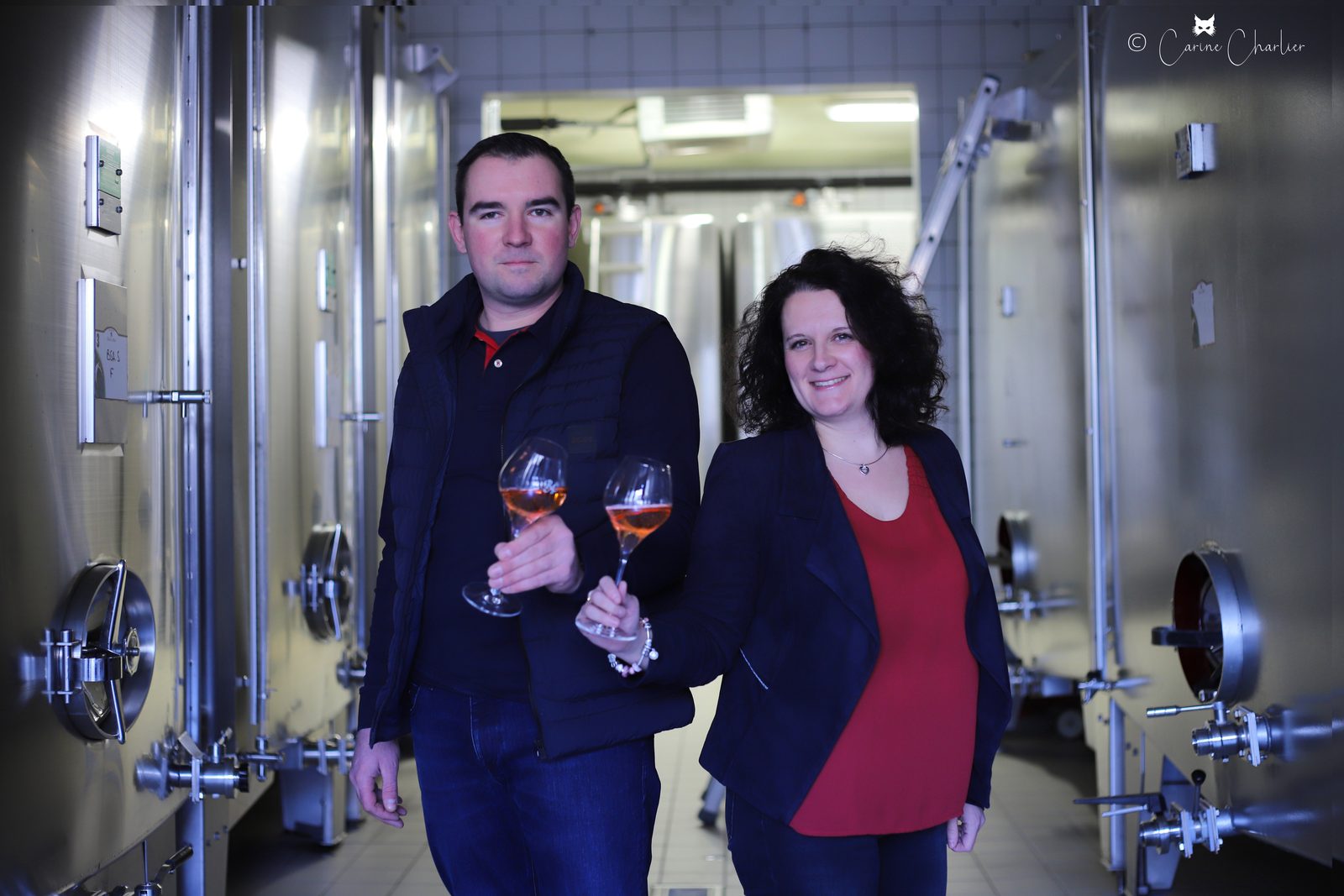 The management of Champagne Robert-Allait in the cellar between stainless steel tanks, each holding a glass of rosé champagne